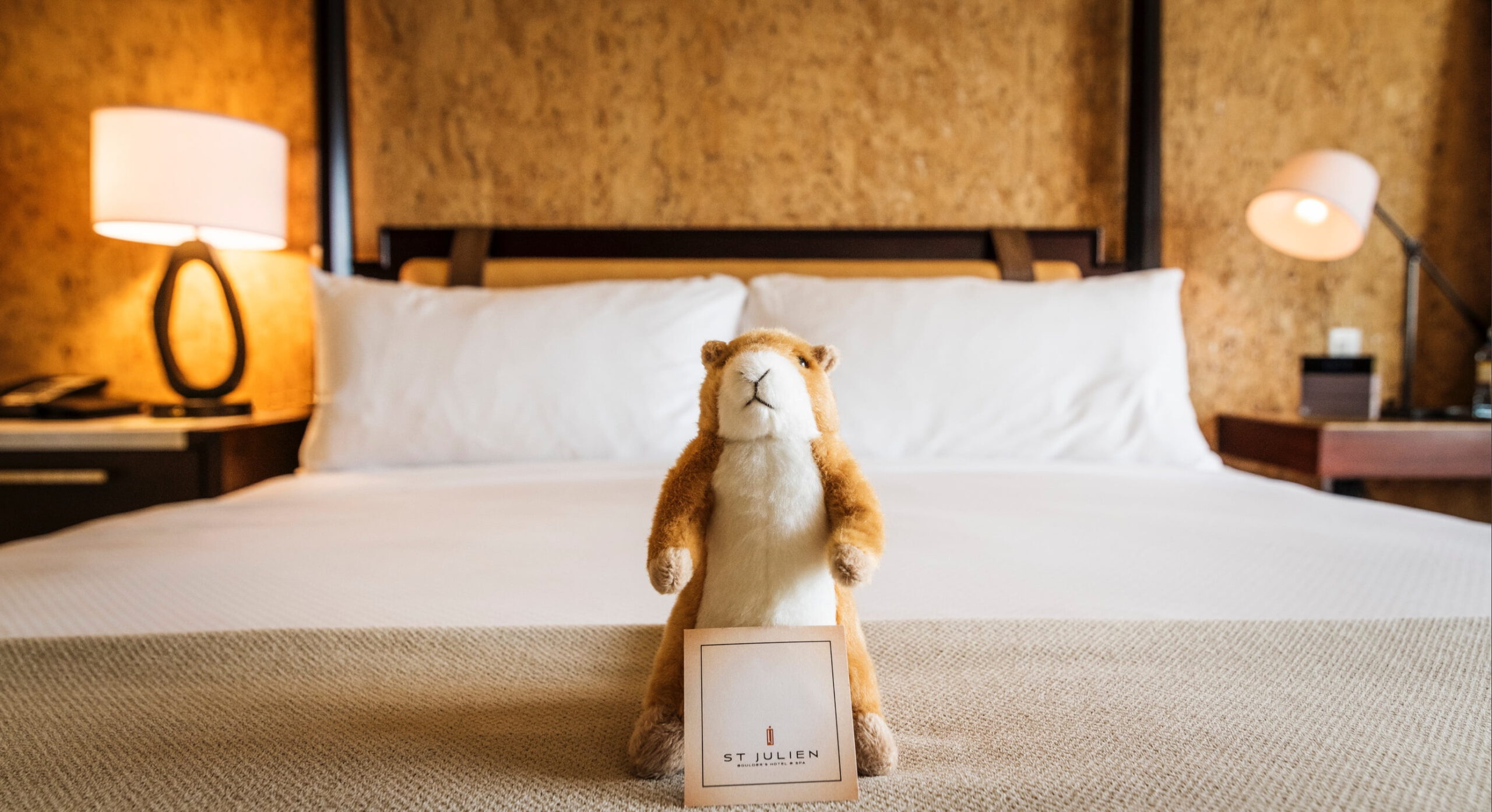 Cute stuffed animal holding a welcome card on a hotel bed