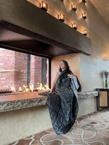Woman by a grand fireplace with a branded blanket.