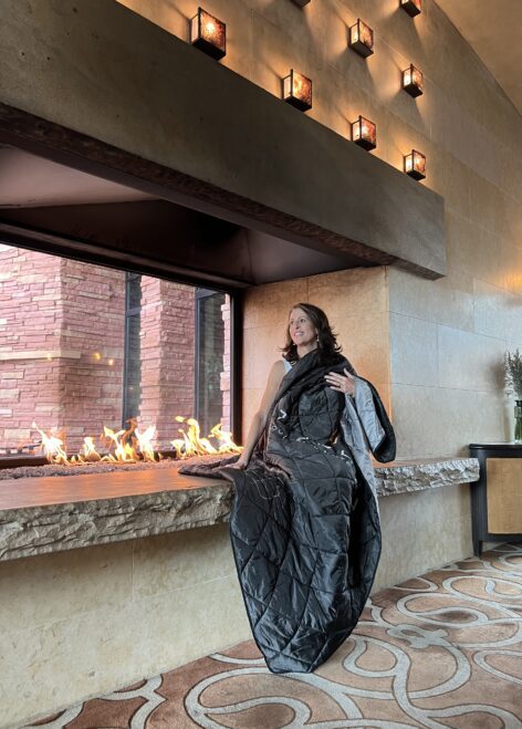 Woman by a grand fireplace with a branded blanket.